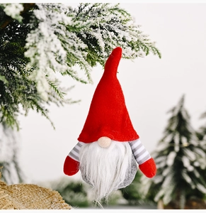 Close-up of festive gnome ornament with red plush hat and white beard on snowy pine branch