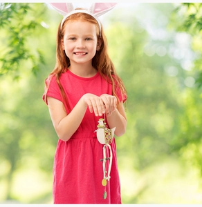 Close-up of wooden Easter rooster pendant with floral cutouts and green ribbon held by a girl