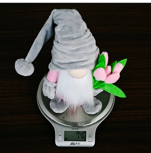 Gnome plush toy with pink tulips weighed on a scale to show its light 74g weight