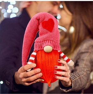 Close-up of knit Valentine gnome with red heart being held by a couple in warm light