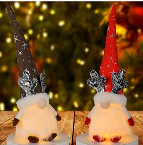 Close-up of glowing Christmas gnomes with reindeer antlers and LED lights on wooden table