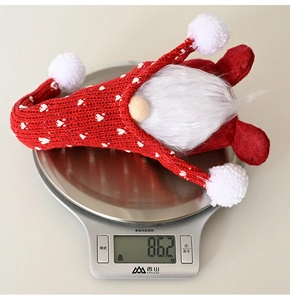 Close-up of a red knitted Christmas gnome on a digital scale showing 86.2g weight