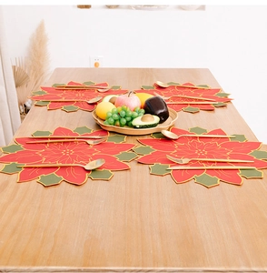 Detailed close-up of four red poinsettia placemats with gold accents on a wooden table