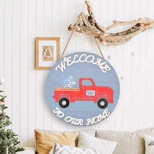 Round wooden Welcome home sign with red truck and snowflakes on a blue background