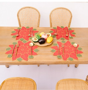 Detailed view of four poinsettia-shaped Christmas placemats with gold stitching on wood table