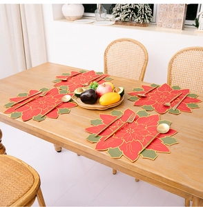 Detailed view of four poinsettia-shaped Christmas placemats on a rustic wooden dining table