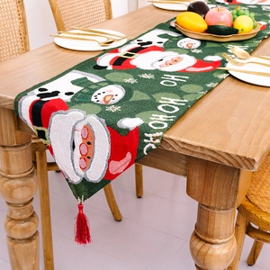Weihnachtstischläufer mit Weihnachtsmann-Motiv, grünem Stoff und roten Quasten auf Holztisch