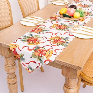 Chemin de table de Noël avec motifs de cloches et pommes de pin sur nappe blanche