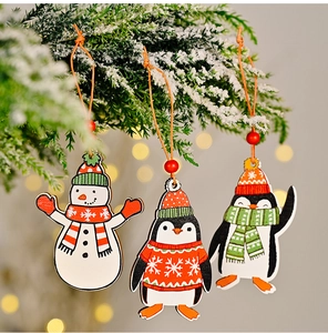 Detail of three wooden Christmas ornaments featuring a snowman and penguins on pine branches