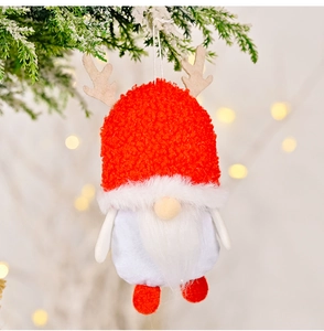 Close-up of Christmas gnome ornament with red plush hat and antlers on snowy pine branch