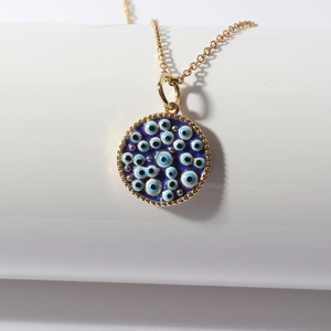 Detailed view of a gold Evil Eye pendant with blue enamel on a minimalist white stand