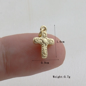 Detailed macro view of a small golden cross pendant with textured finish on a fingertip