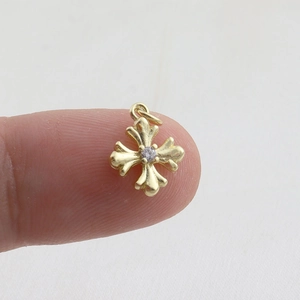 Close-up of a gold cross pendant with fleur-de-lis details held for size comparison