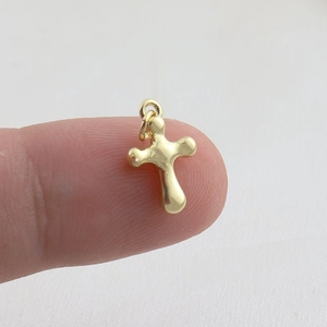 Detailed macro view of a tiny gold-plated cross pendant held on a fingertip for scale