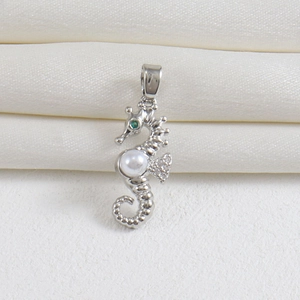 Macro detail of silver seahorse pendant with white pearl and green gemstone eye