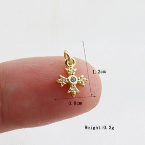 Detailed view of a gold cross charm with white zircons held between fingers for scale