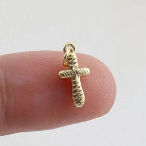 Detailed view of a gold baguette cross pendant held to show the small DIY jewelry scale