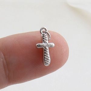 Macro shot of a small silver cross charm with spiral texture held on a fingertip