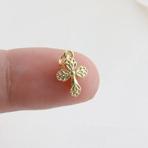 Close-up of a small gold cross pendant with leaf design held on a fingertip