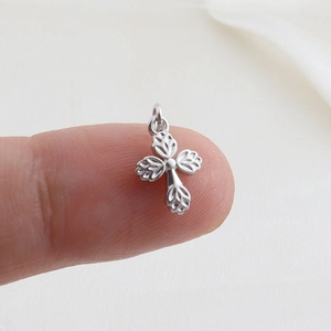 Macro detail of a small silver cross charm pendant held on a fingertip for size scale