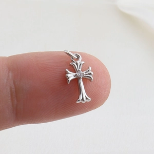 Macro shot of a small silver cross pendant with a center zircon on a fingertip