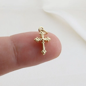 Macro detail of a small gold-plated cross pendant with fleur-de-lis ends on a fingertip