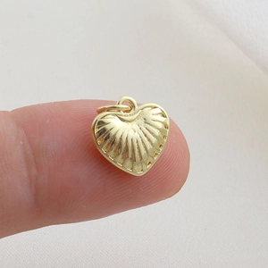 Detailed view of a gold heart pendant with radial textures shown next to fingers