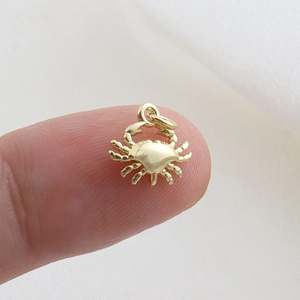 Polished gold crab pendant charm on a fingertip showing its miniature size and detail