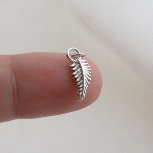 Macro shot of tiny silver feather pendant held by fingertips for size comparison