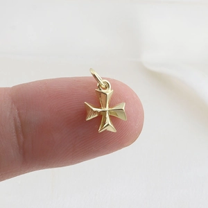 Detailed macro view of a gold Maltese cross pendant held on a fingertip for size reference