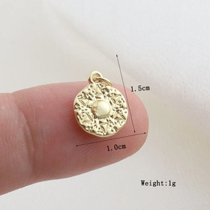 Detailed view of a 1.0cm gold-plated round sunburst charm shown for size on a fingertip