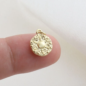 Macro view of a gold-plated brass starburst pendant held on a fingertip for size