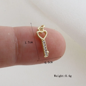 Macro shot of gold-plated heart key pendant with crystals held by fingers for size
