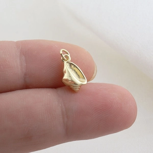 Detailed view of a small gold conch shell pendant held by hand for size reference