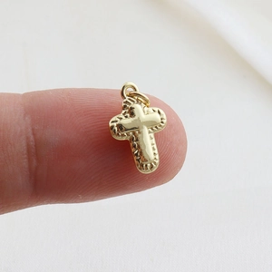 Exquisite gold-plated cross pendant for DIY jewelry making held on a fingertip