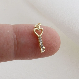 Macro shot of tiny gold-plated heart key pendant with micro-inlaid zircons on a finger