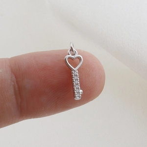 Macro shot of silver heart key pendant with sparkling cubic zirconia on fingertips