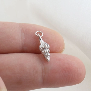 Macro view of a tiny silver seashell pendant held on a fingertip for size scale