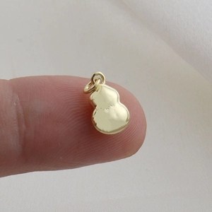 Miniature gold gourd-shaped copper pendant on a finger showing its delicate small size