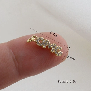 Detailed view of LOVE letter charm with white zircons held by fingers for size scale