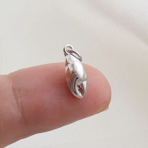 Macro view of a silver crab claw pendant held on a fingertip for size reference