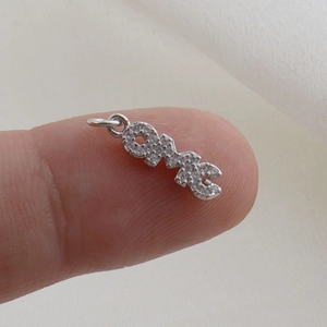Macro view of micro-paved OMG letter pendant in silver tone held by fingertips