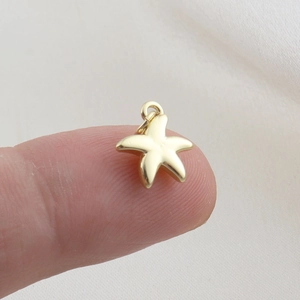 Macro detail of a small gold starfish pendant charm held on a fingertip for scale
