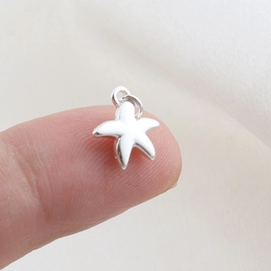 Close-up of a tiny polished silver starfish pendant accessory on a fingertip