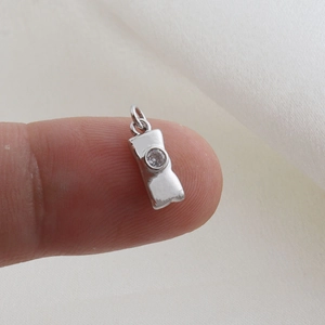 Macro shot of tiny silver padlock charm with zircon inlay held on a fingertip