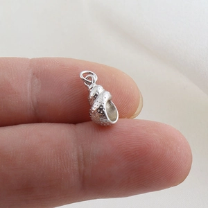Macro view of a tiny silver conch seashell pendant for DIY jewelry on a fingertip