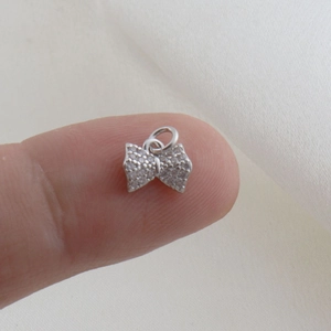 Macro detail of a mini bow charm with pavé zircon setting shown on a fingertip
