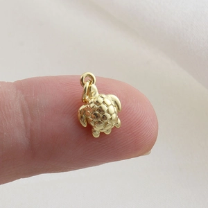 Macro view of a tiny gold turtle pendant with detailed shell texture on a fingertip