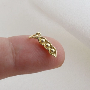 Detailed macro view of a tiny golden pea pod pendant charm held on a fingertip