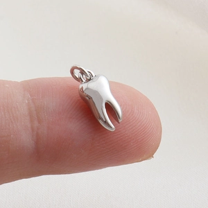 Macro shot of a tiny silver tooth charm held on a fingertip showing precise scale and detail